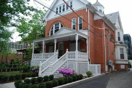A red brick Victorian house with a white porch and front steps, part of Elm Campus housing