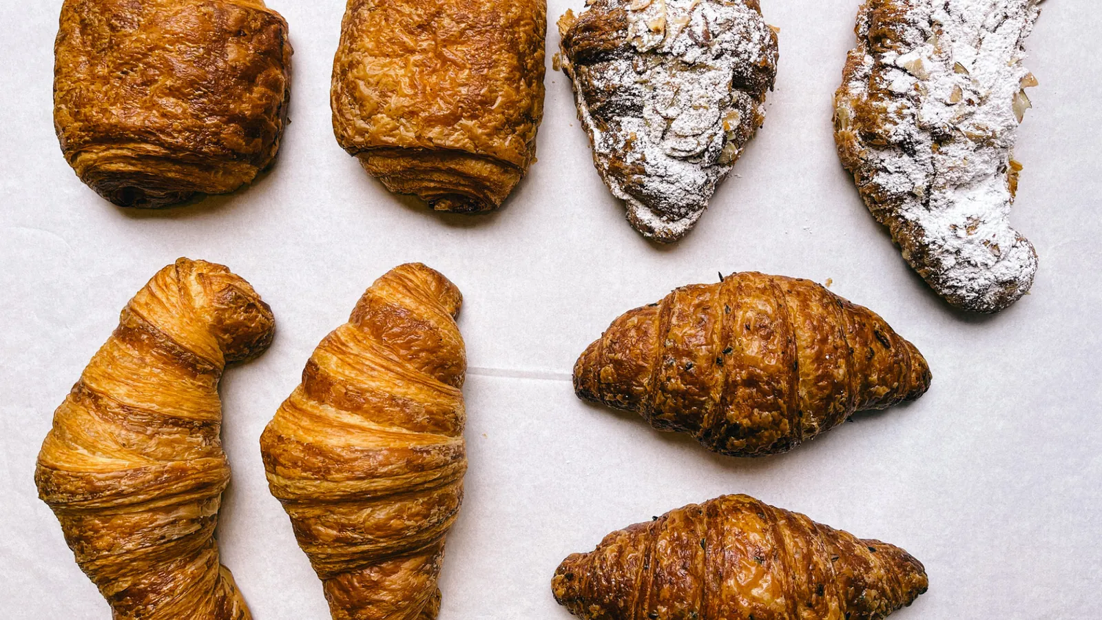 Croissants, pain au chocolat and almond pastries laid out in rows on white paper at G Cafe Bakery
