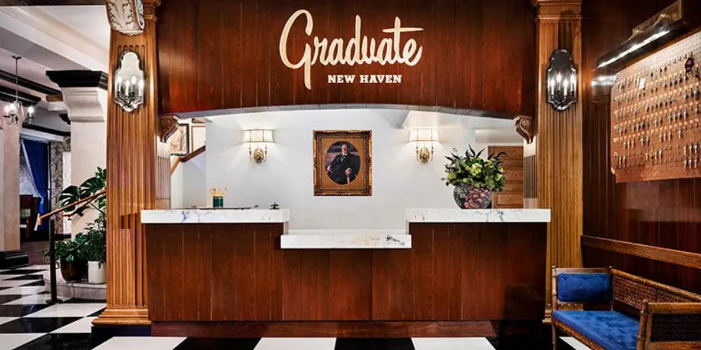 The Graduate New Haven's reception desk in dark panelled wood, a chequerboard floor and the hotel's script sign above