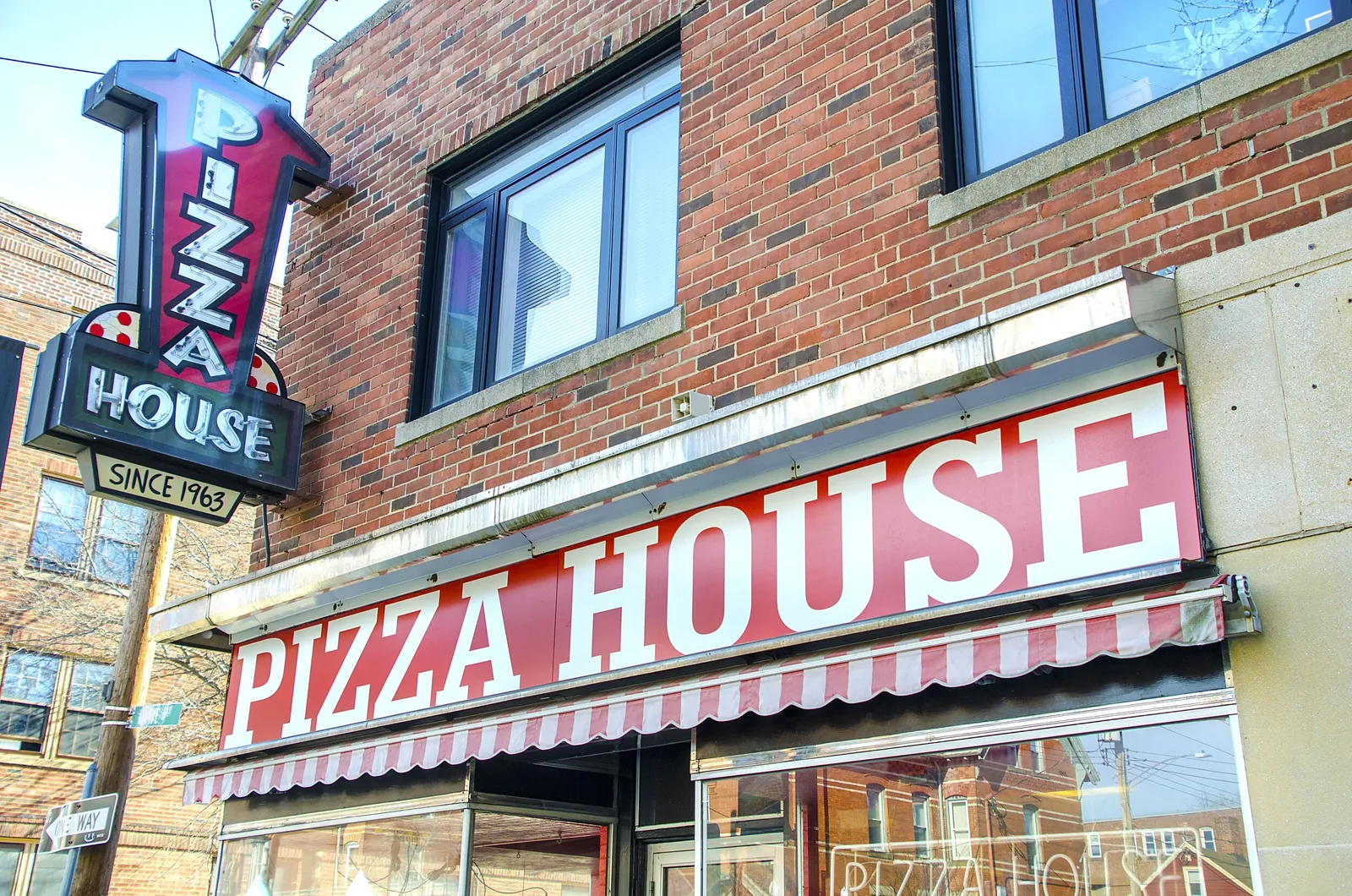 The red awning and vertical neon sign of Pizza House, serving Chapel West since 1963