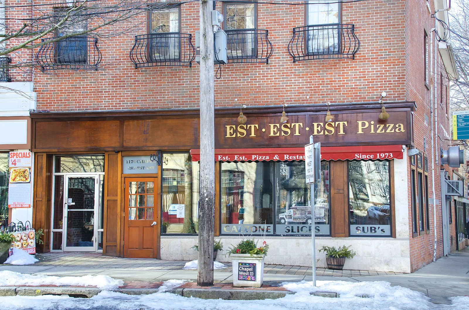 The brick corner storefront of Est Est Est Pizza, snow banked along the sidewalk