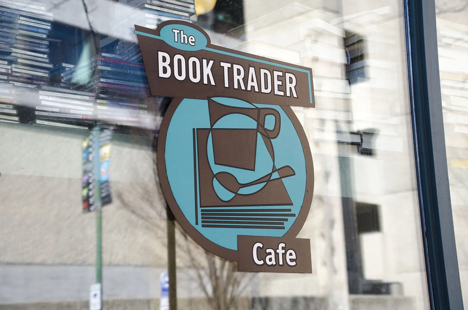The Book Trader Cafe's hanging sign, a book and coffee cup on a teal ground