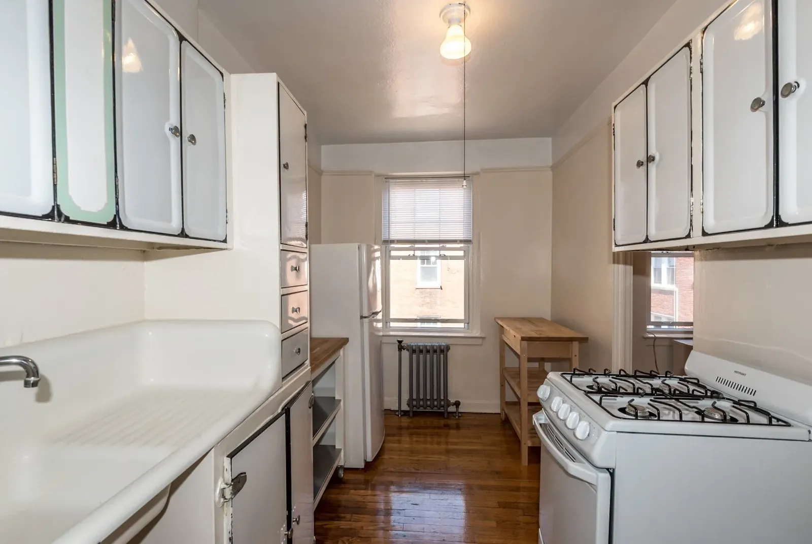A narrow galley kitchen with white cabinets and a gas range in a Howe Place apartment