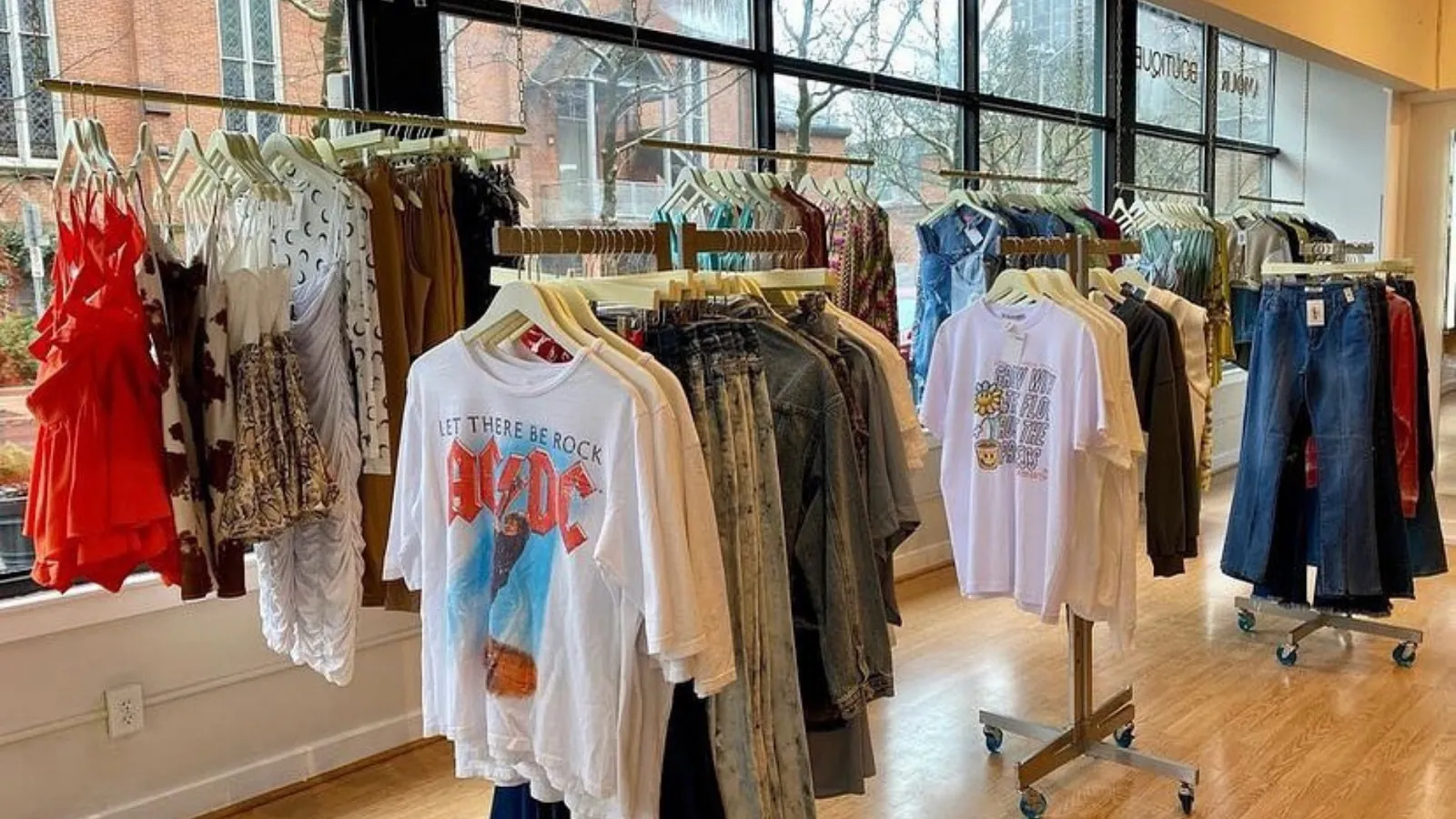 Rails of clothing at More Amour Boutique, printed tees and denim in front of tall shop windows