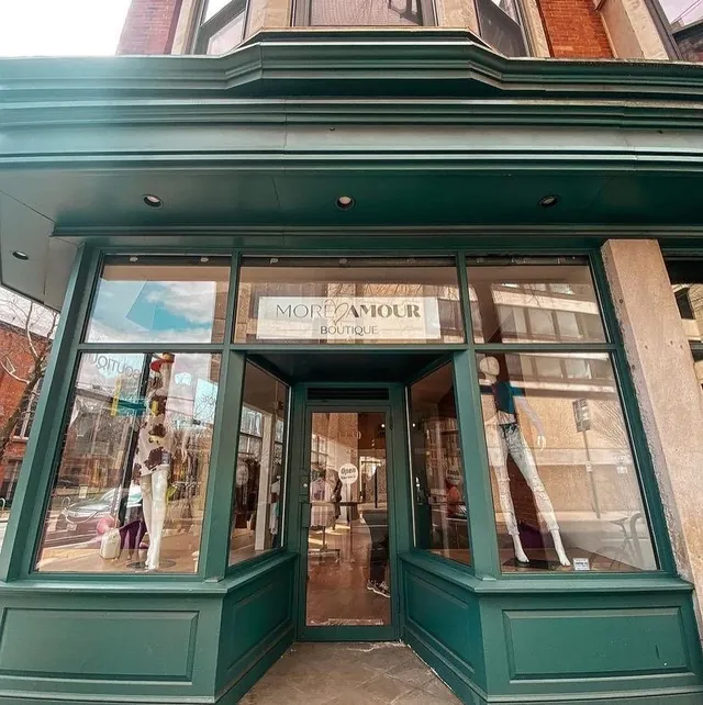 The corner storefront of More Amour Boutique, painted deep green, with dressed mannequins in its two bay windows and the shop's name lettered above the door.