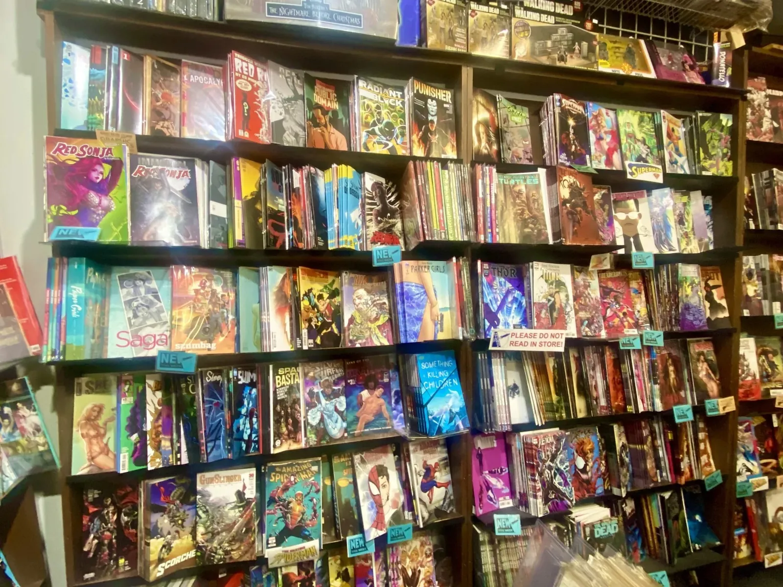 A wall of comic books at Alternate Universe, six shelves deep, packed with titles and hand-lettered section tags.
