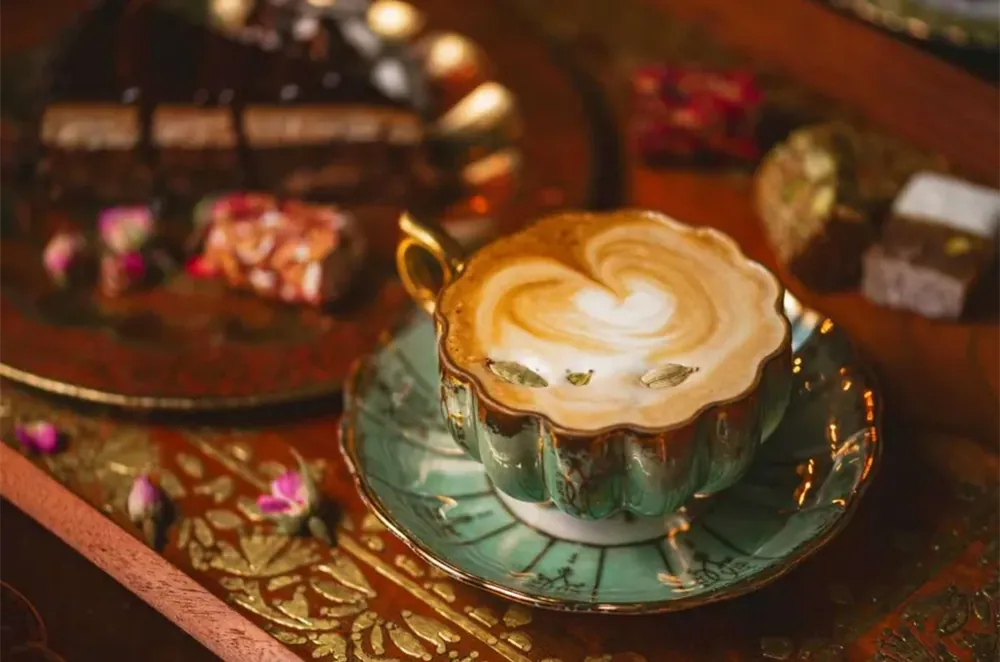 A latte with heart-shaped art in a green and gold cup, served on an ornate tray with sweets at Pistachio