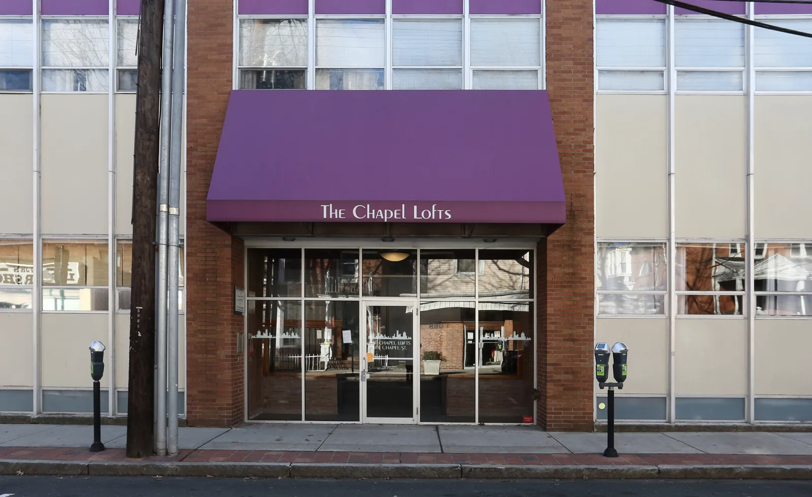 The Chapel Lofts' purple awning above a glass entrance, set into a long tiled facade