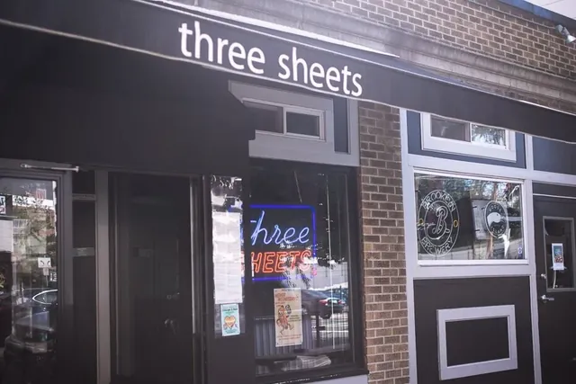 The three sheets sign above the bar's black storefront, its neon sign glowing in the window