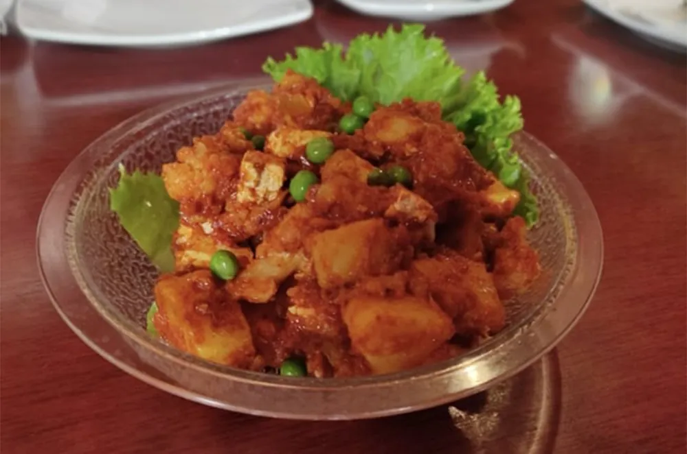 A dish of potato, cauliflower and peas in a red curry, served on lettuce in a glass bowl at Tibetan Kitchen