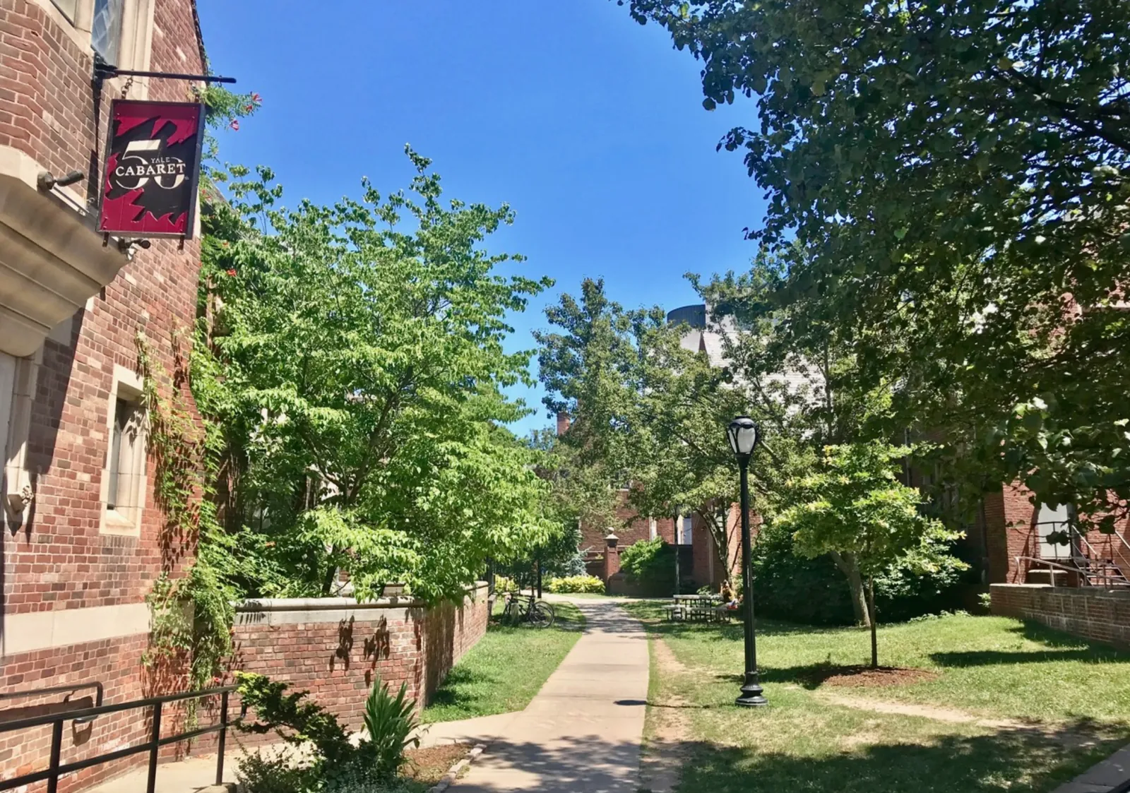 The Yale Cabaret's hanging sign on a brick wall, beside a tree-lined path between buildings